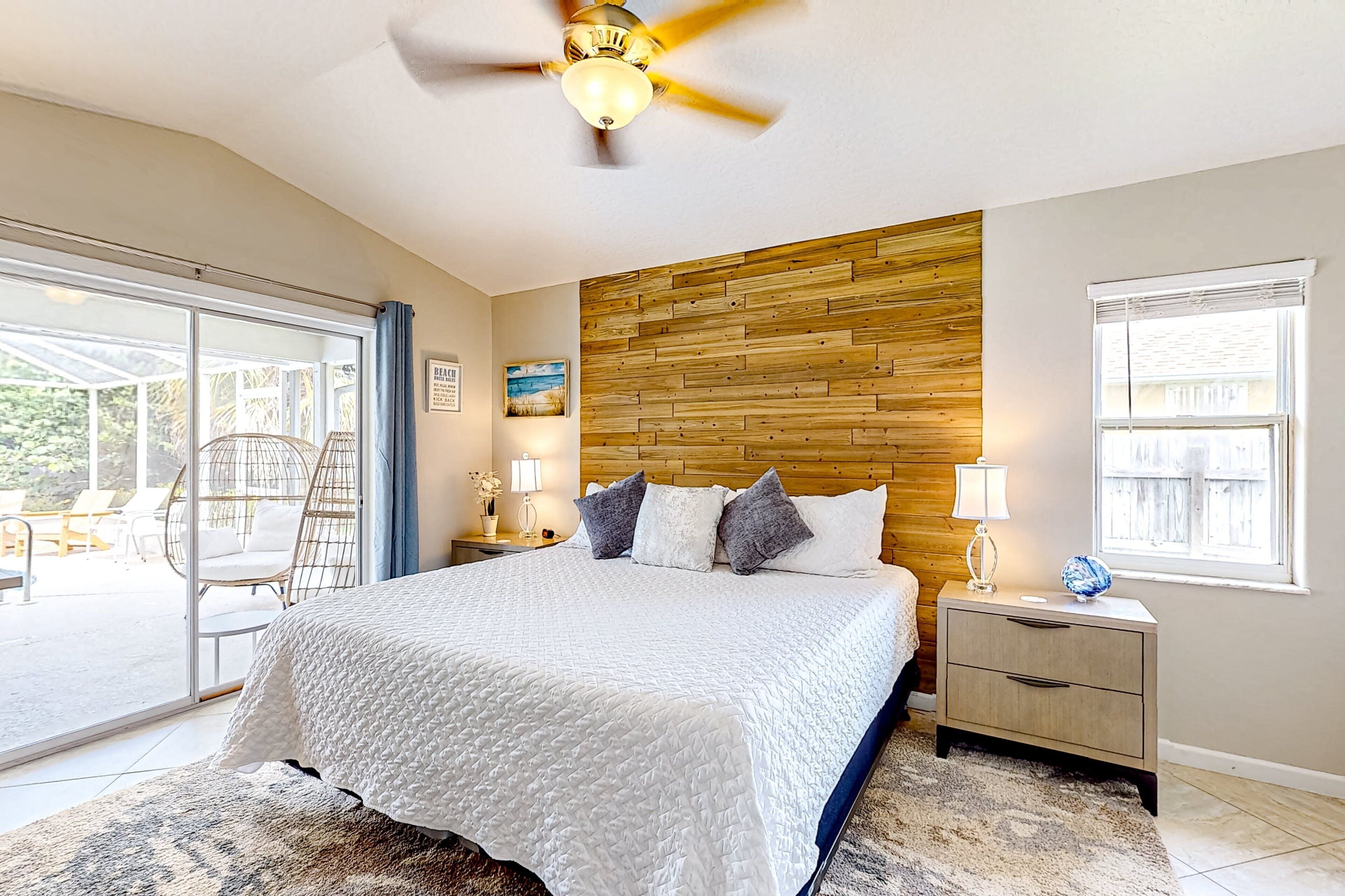 A bedroom with a bed, a wooden headboard, a ceiling fan, a nightstand, and a window.
