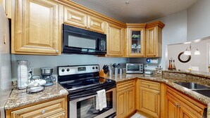 A kitchen with wooden cabinets, a microwave, stove, oven, granite countertop, and a sink. - Cypress Cove 111 (Melbourne)