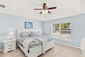 Ein Schlafzimmer mit Bett, Nachttisch, Deckenventilator, Fenster und Kunstwerk.