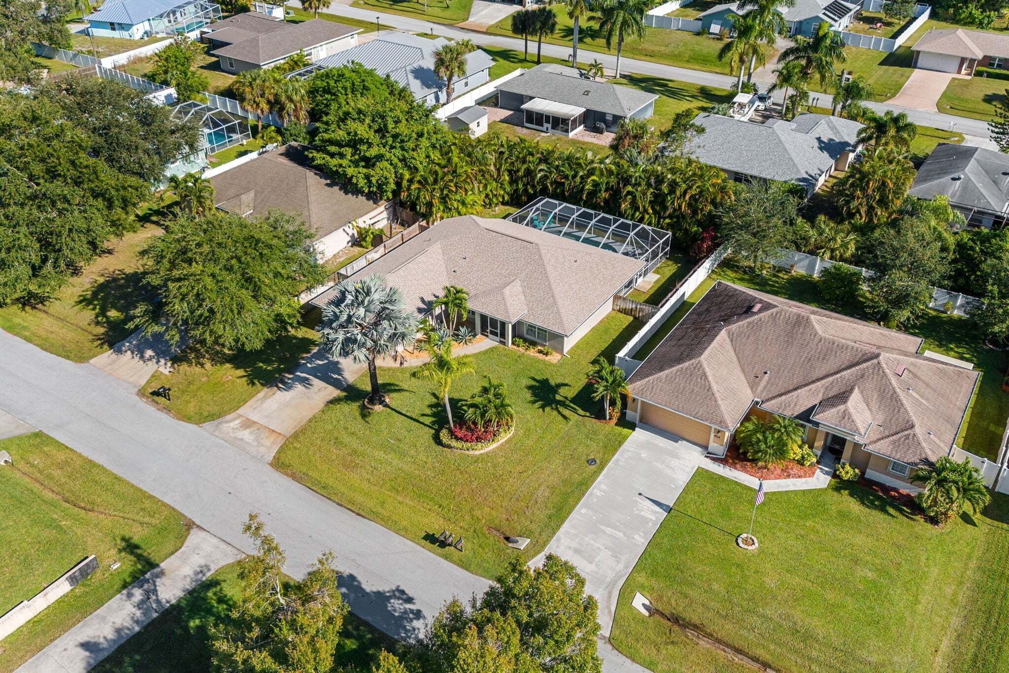 An aerial view of a residential area with houses, green lawns, and palm trees.