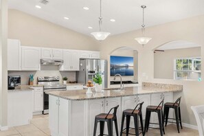 Una cocina moderna con armarios blancos, encimera de granito, electrodomésticos de acero inoxidable y una isla grande con taburetes de bar.