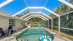 Ein überdachter Pool mit Liegestühlen, klaren Glaswänden und Blick auf Palmen.