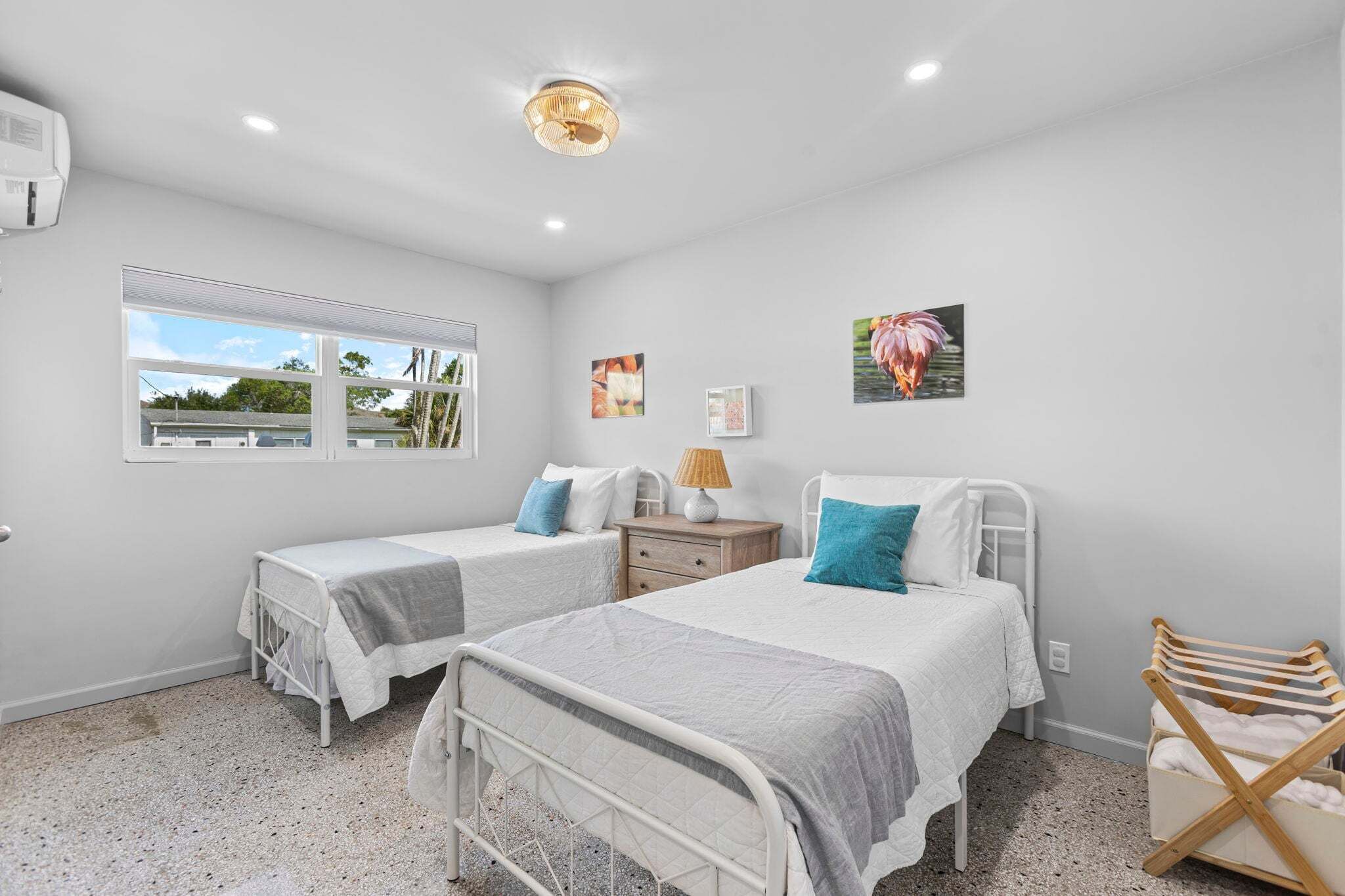 A bedroom with two beds, a window, a ceiling light, and artwork on the walls.