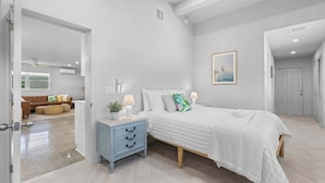 A bedroom with a bed, bedside table, and a view into another room. - Neptune's Hideaway (Vero Beach)