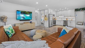 A modern living room with a TV, leather sofas, and a kitchen in the background. - Neptune's Hideaway (Vero Beach)