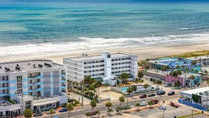 Un hotel sulla spiaggia con diversi piani, una piscina e un'area parcheggio.