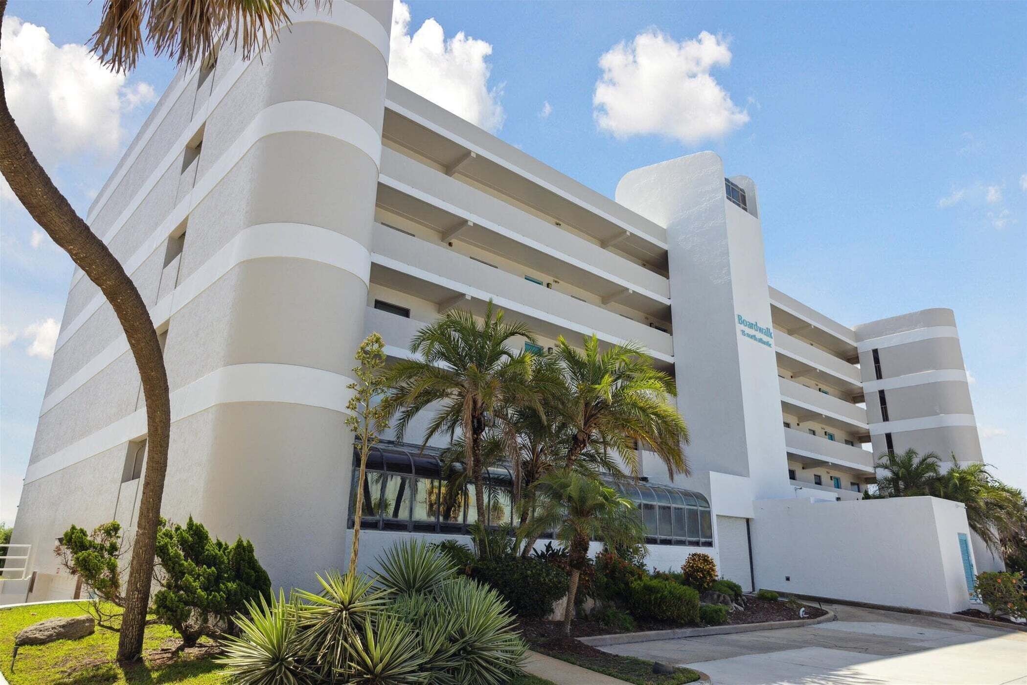 Un hotel de varios pisos con fachada curva, balcones y un patio bordeado de palmeras.
