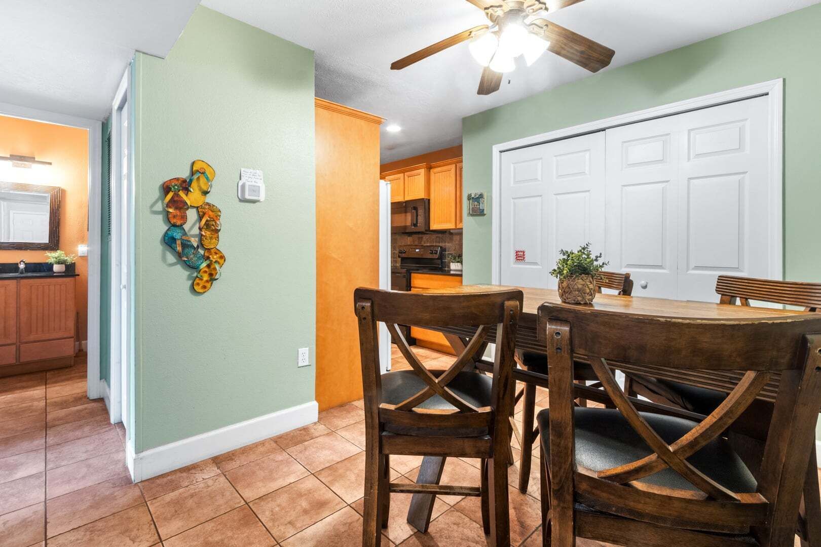 A dining area with a wooden table and chairs, a ceiling fan, and a kitchen in the background.