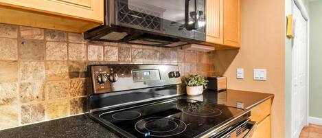 Una cocina con estufa negra, microondas y armarios de madera.