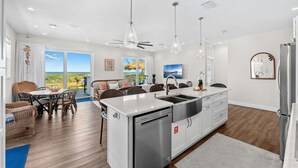 A modern kitchen with a dishwasher, a sink, and a refrigerator. There is a dining area with chairs and a table. - 659 S Atlantic Ave (Cocoa Beach)