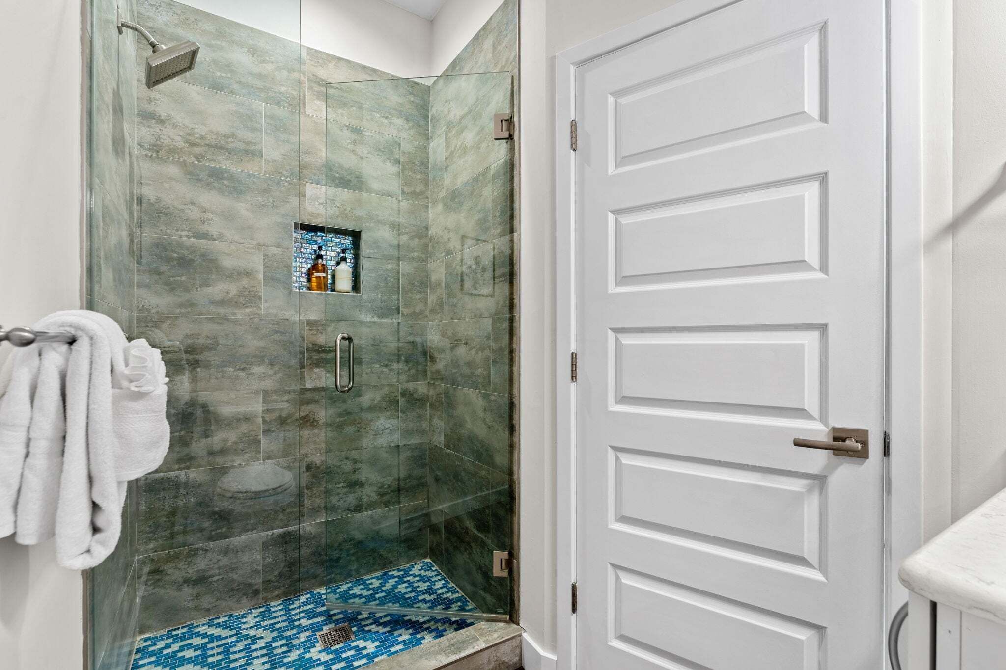 Une salle de bain avec une douche à parois de verre, une porte blanche et un sol carrelé.