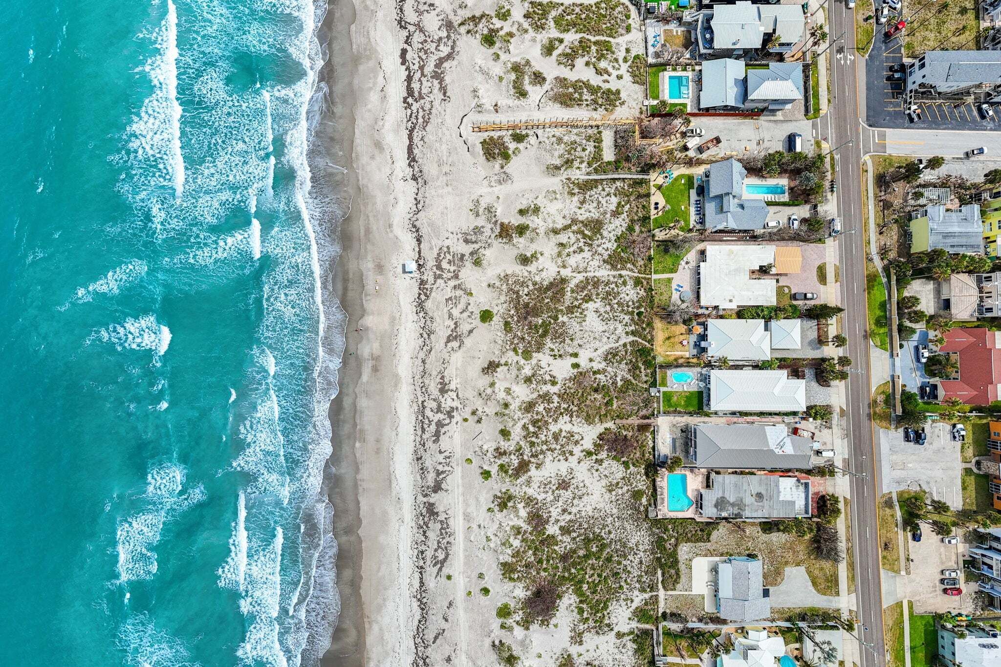 An aerial view of a coastal area with a beach, houses, and a road.