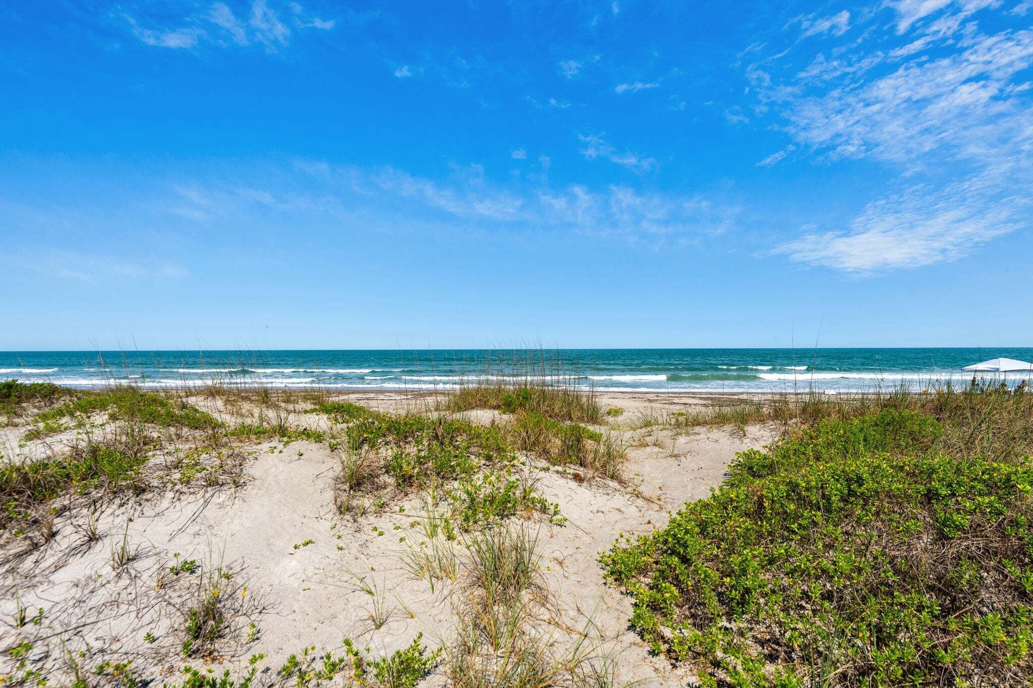 Une plage avec des dunes, l’océan et un ciel dégagé.
