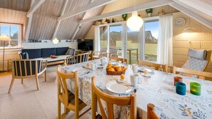 Un comedor con una mesa lista para el desayuno, un sofá y un televisor en un espacio tipo loft con vigas de madera y ventanas amplias.