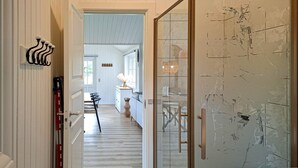 En gang med trappe op til et spiseområde, en glasdør med håndtag, og en vægmonteret lampe.