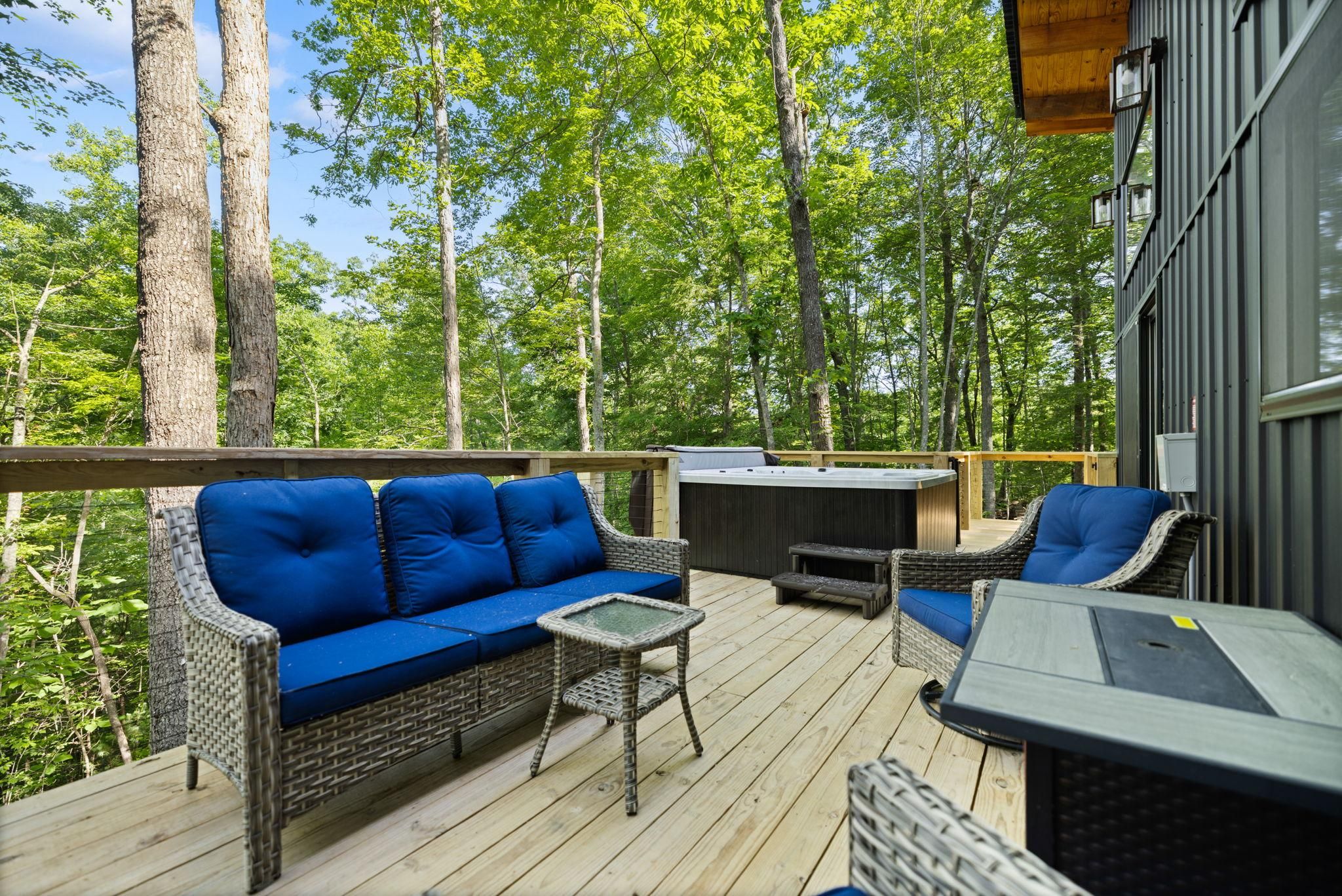 A deck with wicker furniture, a hot tub, and a view of a forest.