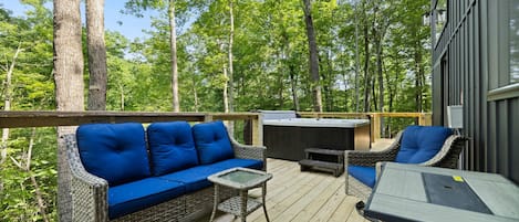 A deck with wicker furniture, a hot tub, and a view of a forest.