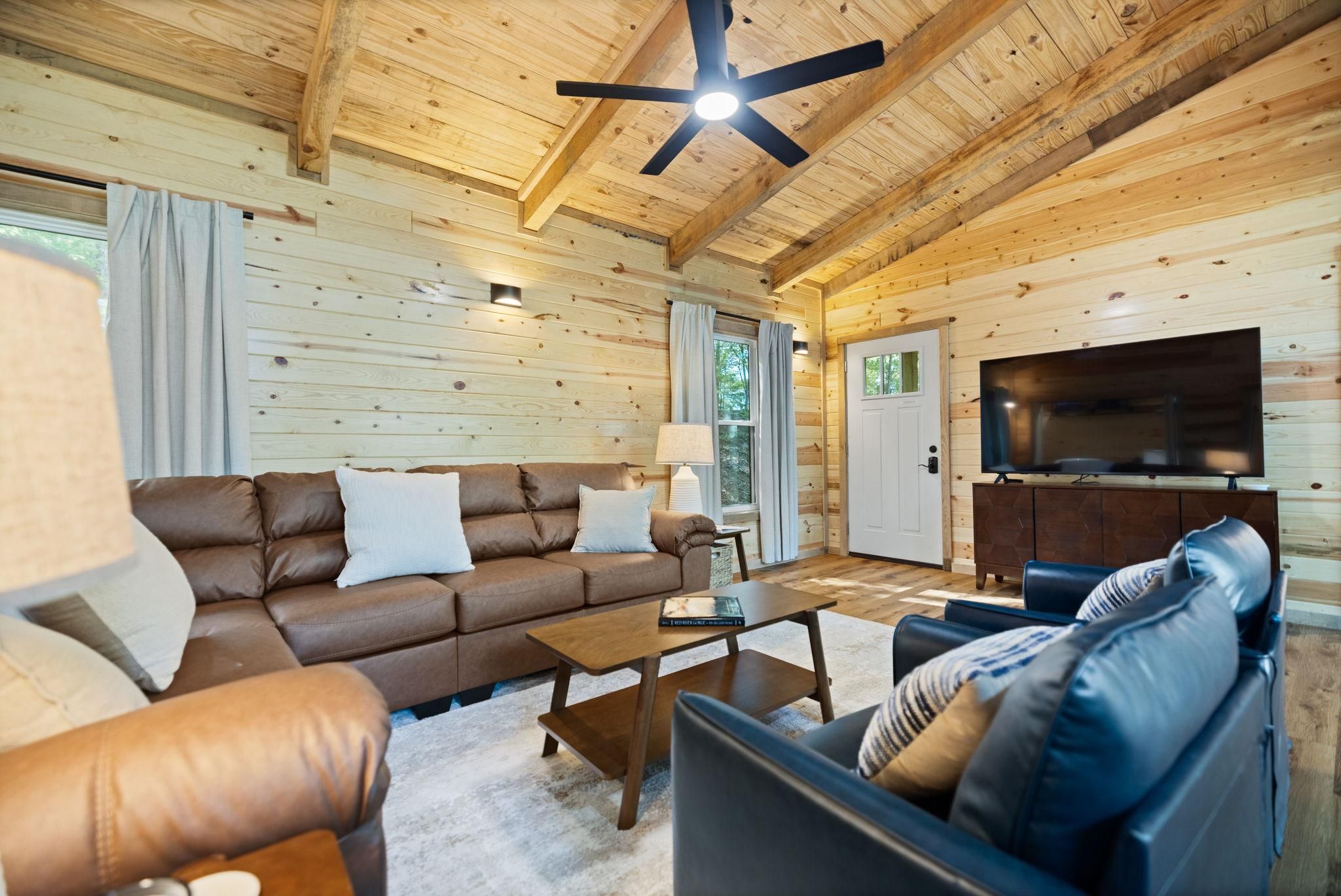 A cozy living room with a brown leather sofa, a blue sofa, a coffee table, and a flat-screen TV mounted on the wall.