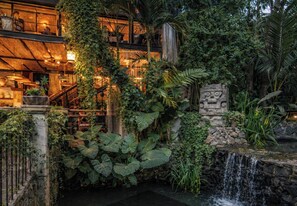 A multi-level building with a waterfall, lush greenery, and a stone wall with a face design.