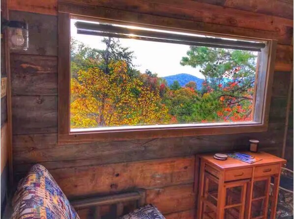 Ein Blockhaus-Innenraum mit Fensterblick auf einen Wald, einer hölzernen Bank und einem kleinen Tisch.