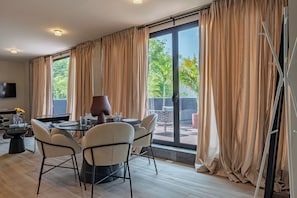 Ein Essbereich mit Tisch und Stühlen, einem Fernseher und Blick auf Grünfläche.