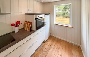 A compact kitchen with white cabinetry, a built-in oven, and a window with a view of trees. - 3 bedroom nice home in Ringkøbing (Ringkøbing)