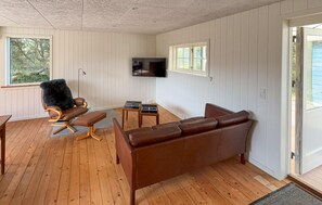 A room with a brown leather sofa, a rocking chair, a TV mounted on the wall, and a window with a view of trees. - 3 bedroom nice home in Ringkøbing (Ringkøbing)
