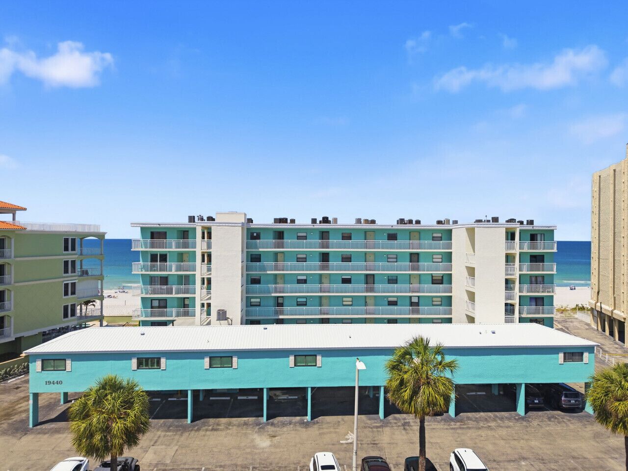 Un hôtel à plusieurs étages, doté d’un parking à l’avant, offrant une vue sur la plage et surplombant un ciel dégagé.