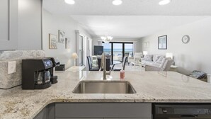 A modern kitchen with a built-in dishwasher, a coffee machine, and a large island with a sink. - Amazing 1 bedroom with Gulf Views and Wraparound Balcony (Indian Shores)