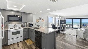 A modern kitchen with a microwave, stove, and dishwasher, a dining area with a table and chairs, and a balcony with a view of the ocean. - Amazing 1 bedroom with Gulf Views and Wraparound Balcony (Indian Shores)