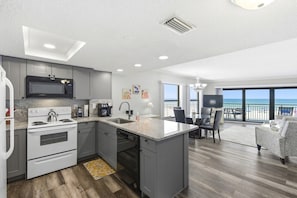 Eine moderne Küche mit Mikrowelle, Herd und Geschirrspüler, ein Essbereich mit Tisch und Stühlen und ein Balkon mit Meerblick.