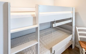 Ein Etagenbett mit einem unterem Bett und einer ausziehbaren Schublade, ein weißer Stuhl und ein kleiner Tisch.