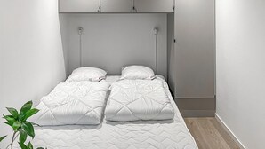 Een enkel bed met een wit geborduurde matras en twee kussens, een klein nachtkastje en een wandkast boven het bed.