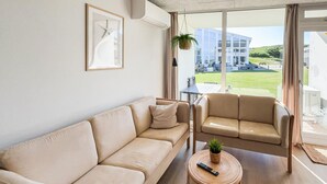 Een woonkamer met een bank, een stoel, een klein tafeltje met een afstandsbediening en een hangplant.