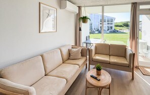 Ein Wohnzimmer mit einer Couch, einem Sessel, einem kleinen Tisch mit Fernbedienung und einer hängenden Pflanze.