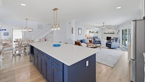 A spacious kitchen with a large island, a dining area with wooden chairs, a living room with a sofa and armchairs, and a view of the outdoors through large windows. - Waterfront Home with Pool in Redington Beach (Redington Beach)