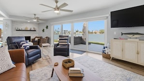 A spacious living room with a large window, a flat-screen TV, and a ceiling fan. - Waterfront Home with Pool in Redington Beach (Redington Beach)