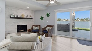 A living room with a fireplace, two wicker chairs, a sofa, a ceiling fan, and a large sliding glass door with a view of a body of water and palm trees. - Waterfront Home with Pool in Redington Beach (Redington Beach)