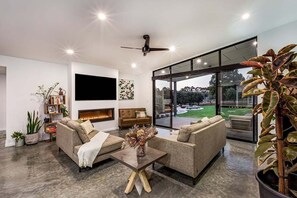 A modern living room with a fireplace, sofas, a coffee table, and a large window offering a view of the outdoors.