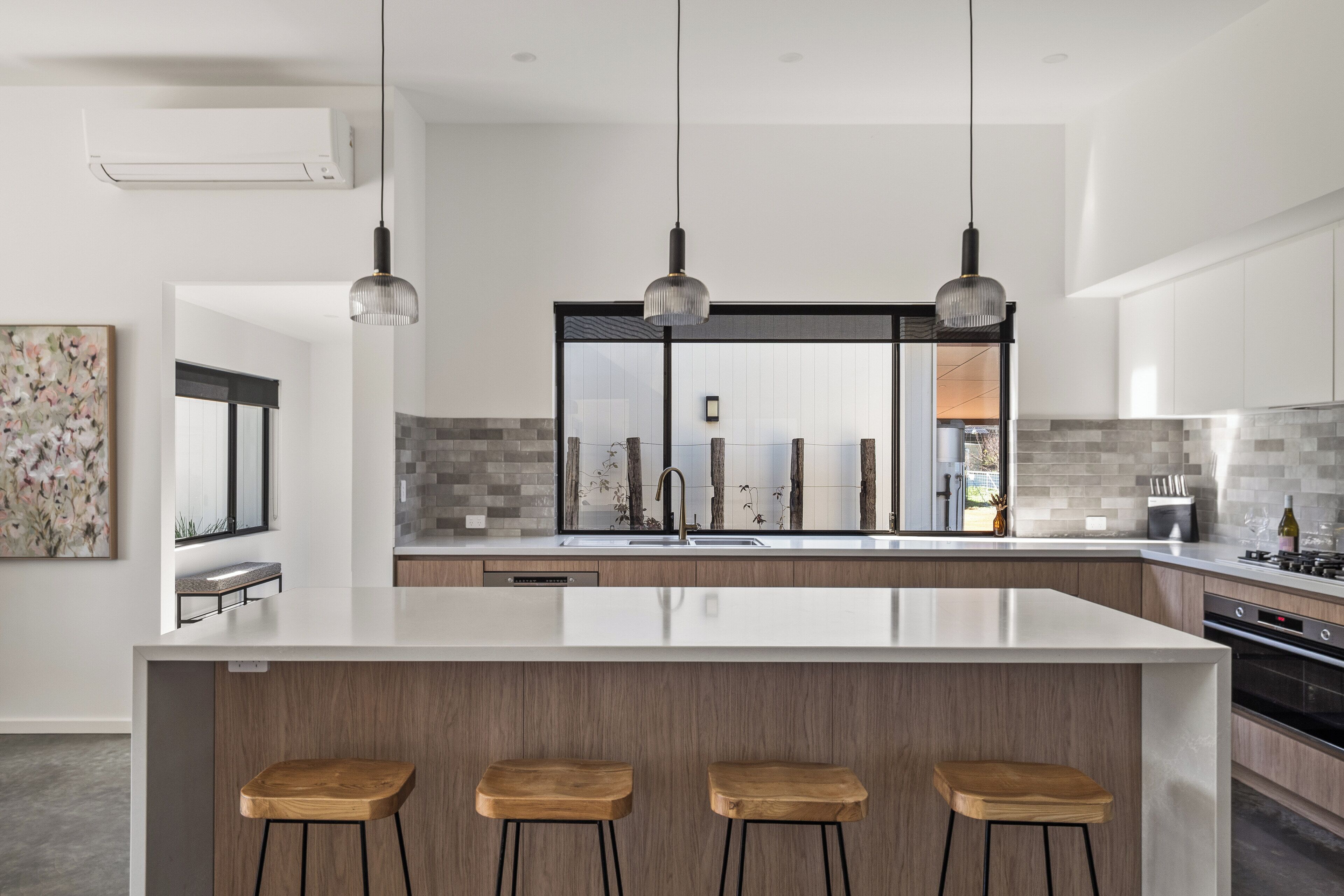 A modern kitchen with a large island, pendant lighting, and a view into the living area.