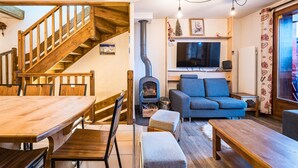 Een gezellige woonkamer met een houten trap, een open haard, een bank en een eettafel.