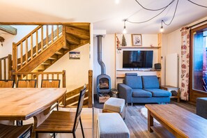 Ein gemütliches Wohnzimmer mit einer Holztreppe, einem Kamin, einer Couch und einem Esstisch.