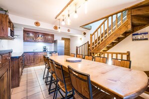 Eine Küche mit Holzausstattung, einem Esstisch mit Stühlen, einem Kühlschrank und einer Holztreppe.