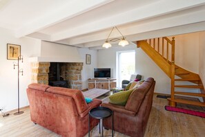 A living room with a stone fireplace, a wooden staircase, and a television. - La Maison de Gianni - 7km de la Plage (Quettreville-sur-Sienne)