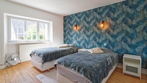 Ein Schlafzimmer mit zwei Betten, einem Fenster, einer Heizung und einer Wandleuchte.