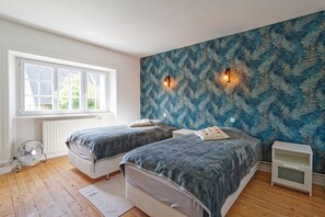 A bedroom with two beds, a window, a radiator, and a wall-mounted light fixture. - La Maison de Gianni - 7km de la Plage (Quettreville-sur-Sienne)