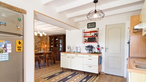 Eine moderne Küche mit weißen Schränken, einem eingebauten Ofen, einem Kühlschrank, einer Steinwand, einem Holzesstisch und einer Pendelleuchte.