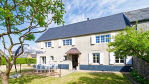 Ein zweistöckiges Haus mit einem geneigten Dach, einer Veranda mit Stühlen und einem gepflegten Rasen.