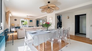 A dining area with a table set for four, clear chairs, and a decorative ceiling fan. - Kerblue - Charmante maison à 3 km de la plage (Carnac)