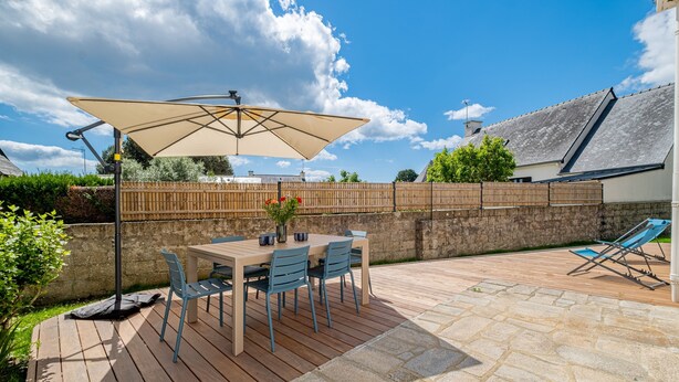 A patio with a table and chairs, a large umbrella, and a stone floor. - Kerblue - Charmante maison à 3 km de la plage (Carnac)
